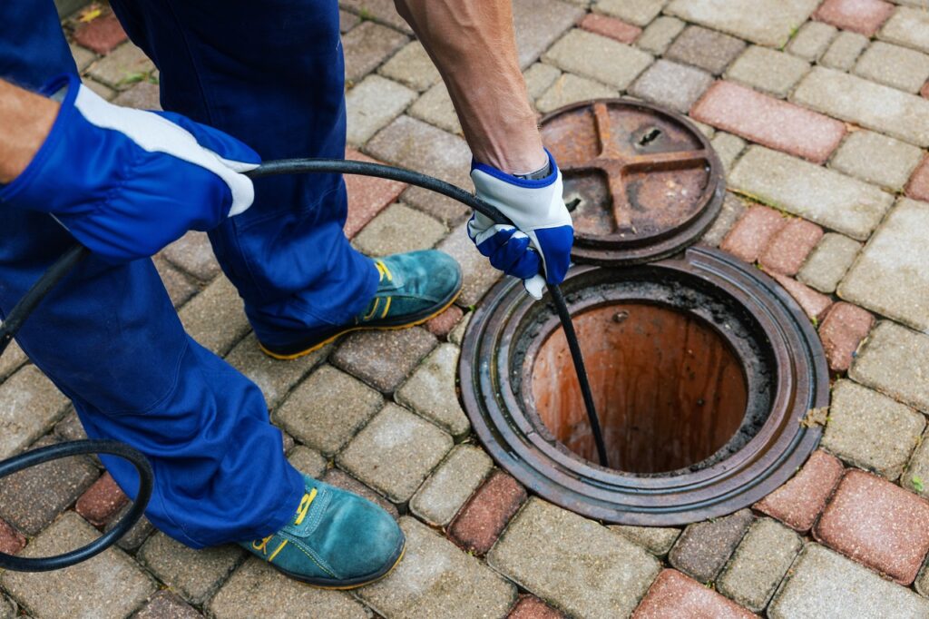 Plumber cleaning outdoor sewer drain with professional cable tool