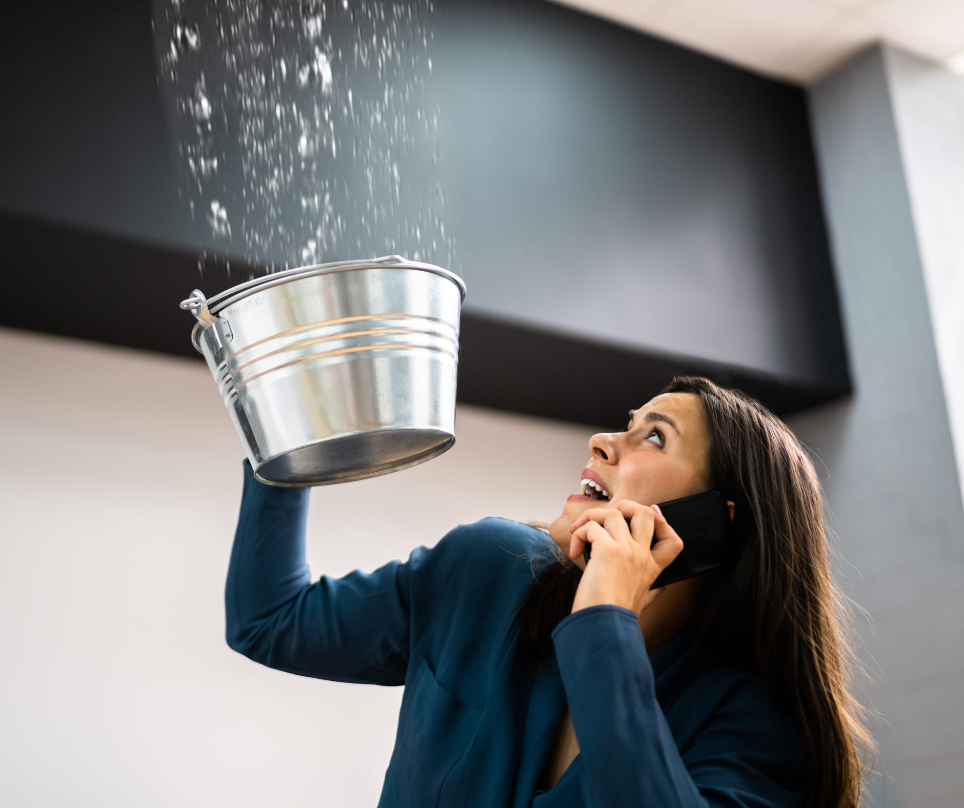 Woman holding bucket under ceiling leak while calling emergency plumber